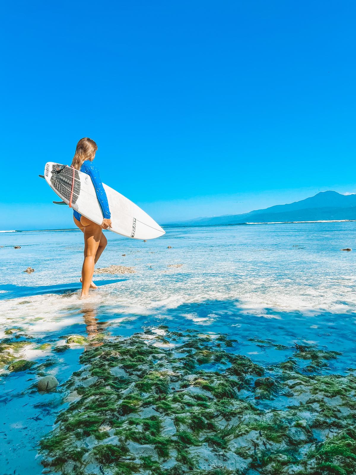 Piper, a beautiful surfer girl, standing in a blue ocean with her surfboard 